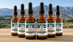 Six bottles of Oregano Oil with droppers on a wooden surface with a mountainous background.